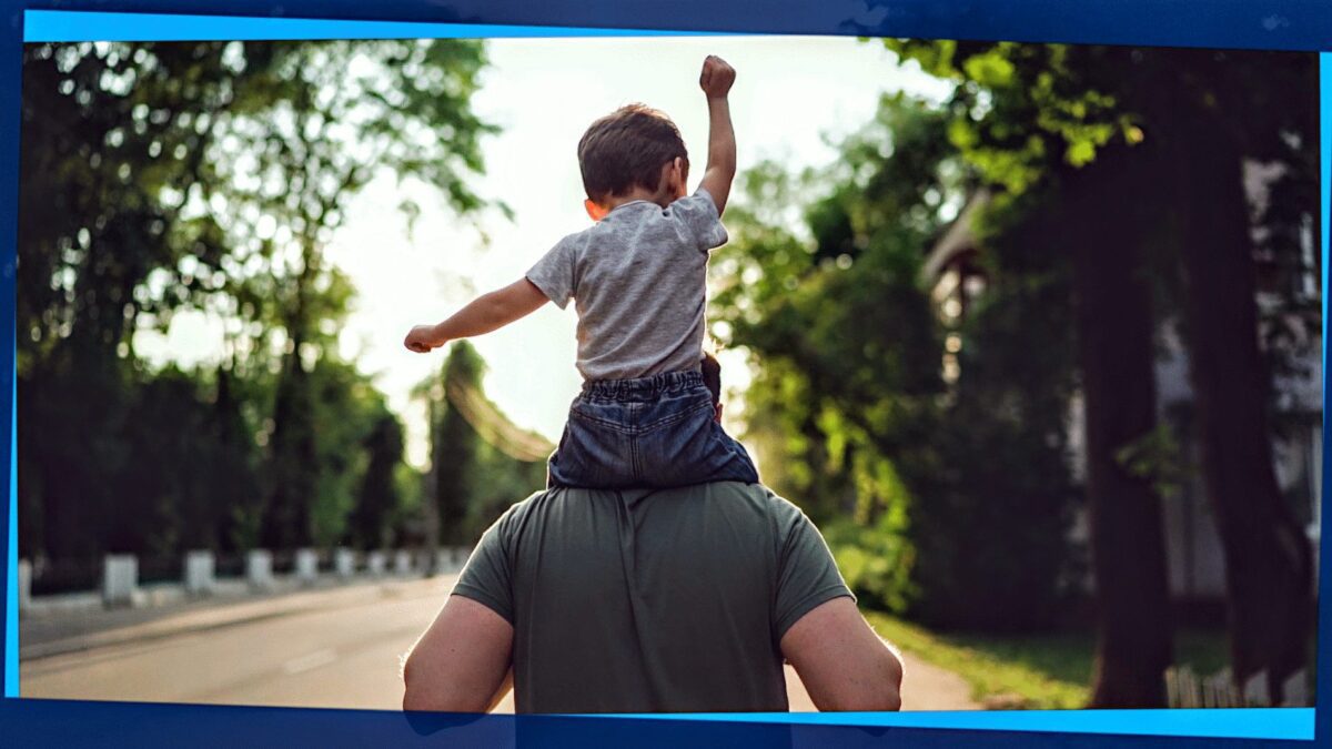 Photo of a 4 year old boy raising his fist while getting a piggy-back ride from his dad
